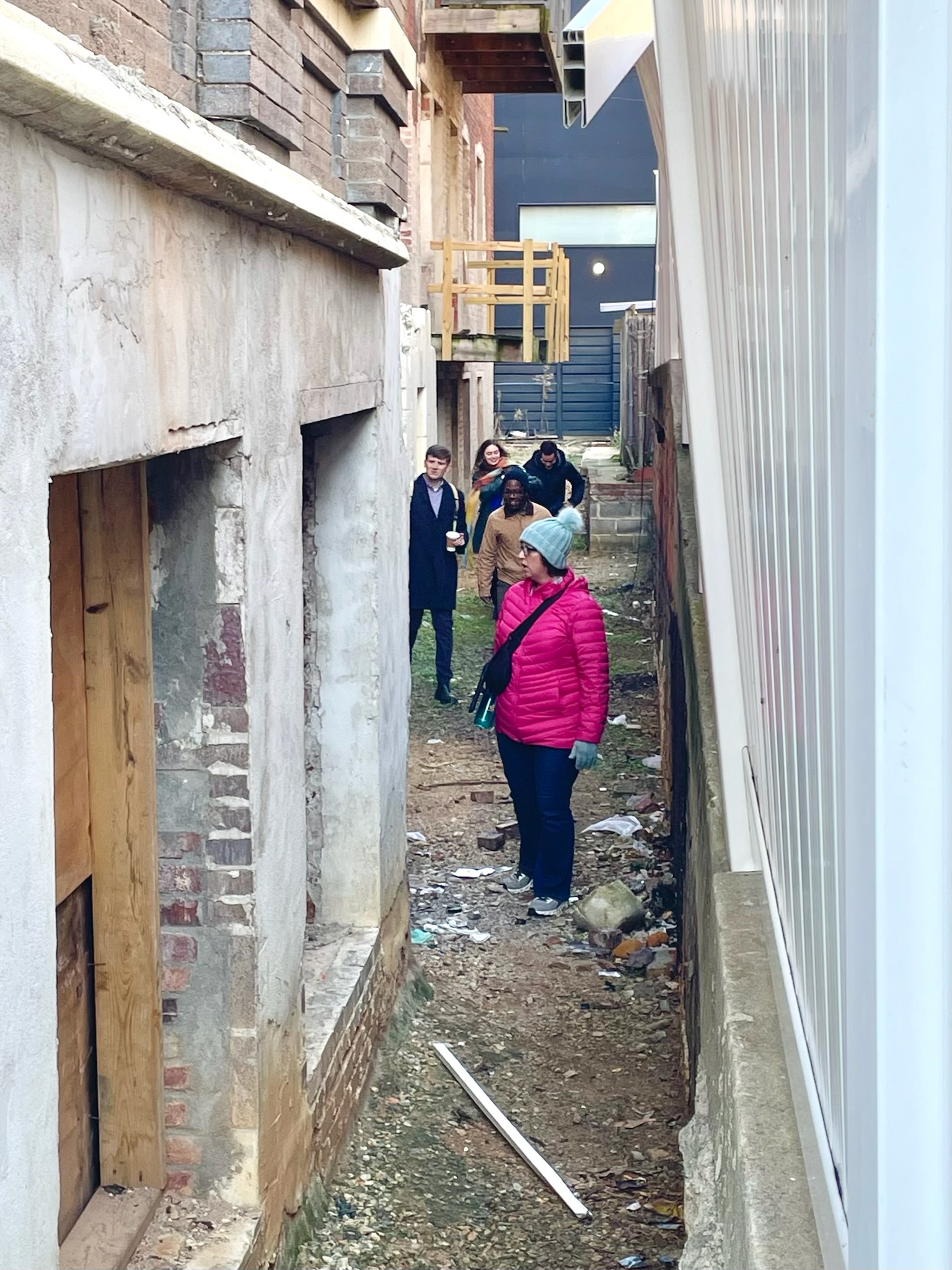 Councilmember Nadeau and others standing in a narrow space between two buildings, looks at the building and boarded up windows.