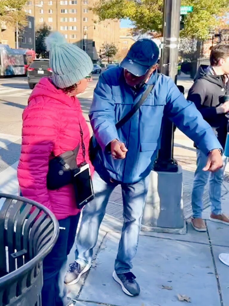 Councilmember Nadeau, wearing a knit cap and pink puffer coat, speaks with a man in a baseball cap who is gesturing and leaning forward.