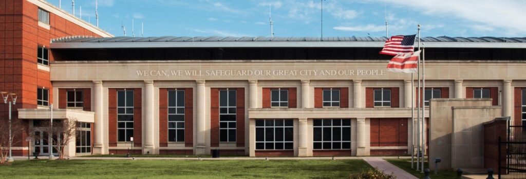 Brick and concrete Office of Unified Communications' building with American flag on a tall pole in front and a grassy area.