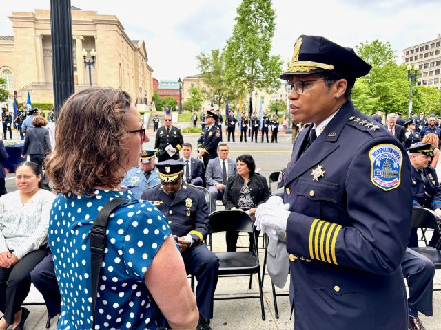 Councilmember Nadeau speaks with MPD Chief Pamela Smith before the ceremony begins; Officers carrying flags and ceremonial rifles march in front of a line of officers in uniform standing at attention; Officers in dress uniform stand and salute. Behind them a row of many other officers do the same. 