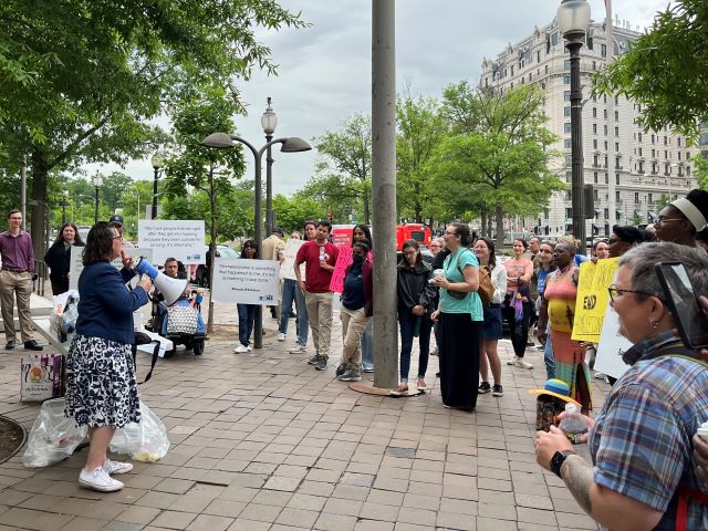 Councilmember Brianne Nadeau speaks into a megaphone outside the Wilson Building in front of advocates holding signs about ending homelessness and supporting funding for housing programs