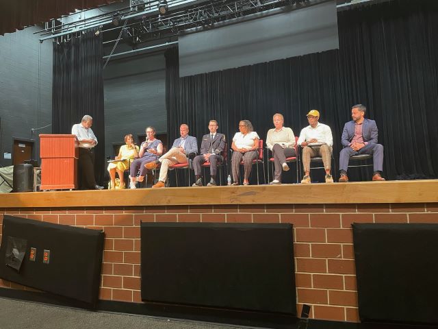 Closeup showing Councilmembers Nadeau speaking while seated onstage with a panel of people.