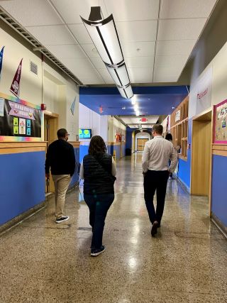 Three individuals walk down the hallway of a school with their backs toward the camera.