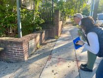 Councilmember Brianne K Nadeau and Councilmember Matt Frumin lean down on a sidewalk to read a plaque on a short brick wall at the entrance to a park