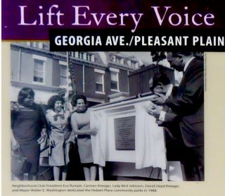 Text at the top of the photo reads Lift Every Voice Georgia Ave/Pleasant Plain. Three women, including Lady Bird Johnson, stand to the left of a plaque that is being unveiled. Two men stand to the right of the plaque and clap their hands. Housing is seen in the background of the photo.