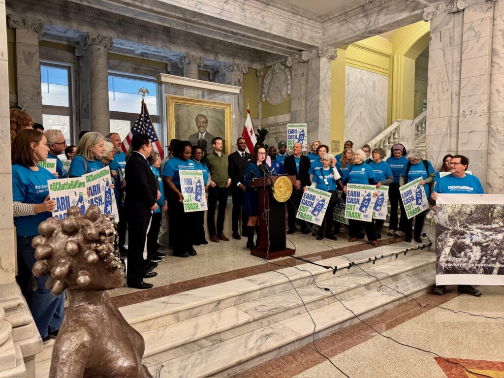 Councilmember Nadeau speaks at press conference at Wilson Building foyer surrounded by advocates in blue t-shirts