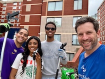 Three college students, one wearing a Howard University sweater and a person in a Brianne K. Nadeau tee shirt pose for a photo outside a building.