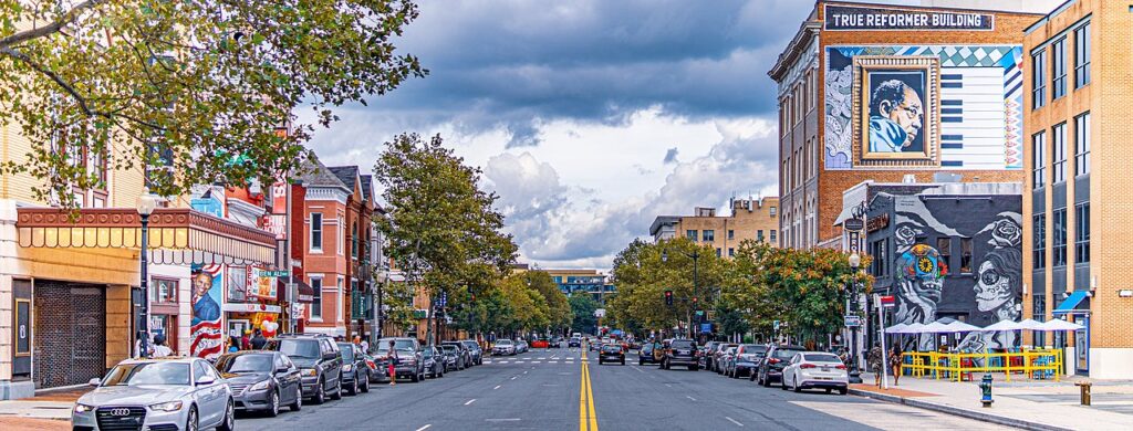View of U St. with cars parked on both sides and buildings, including one with big lettering reading "TRUE REFORMER BUILDING" and a mural. Across the street is Ben's chili bowl, with its iconic awning.