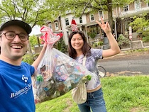 Two people pose for a selfie, one holds a bag of trash