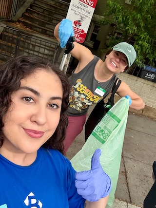 Two people pose for a selfie, one holds up a trash picker and trash bag