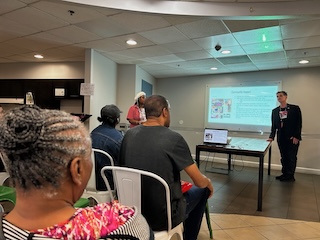 A HIPS staff member presents in front of a video projector screen while other staff members are seated in chairs