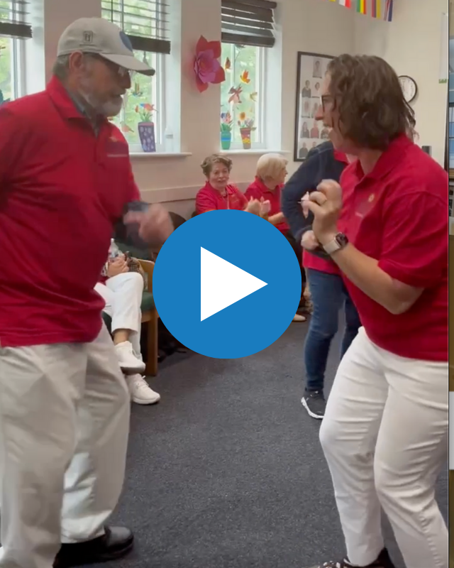 Screenshot of video of gentleman wearing baseball cap and Councilmember Nadeau dancing. Both are wearing matching red shirts as seniors seated in chairs watch and clap, also wearing matching red shirts