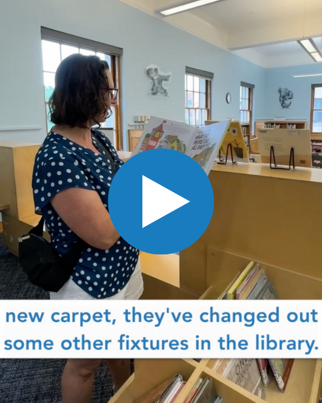 Screenshot from video of Councilmember Brianne Nadeau standing in Mt Pleasant Library children's book section, holding up children's book and reading from it