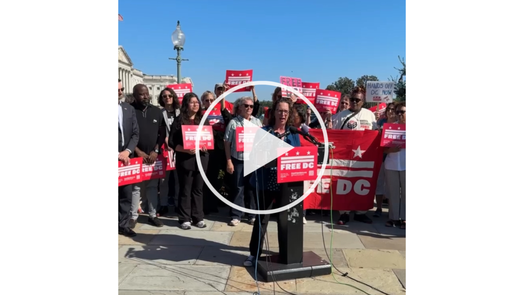 Councilmember Nadeau speaks at a rally on Capitol Hill, in front of a crowd of people holding red Free DC signs. A white "play" button covers the image.