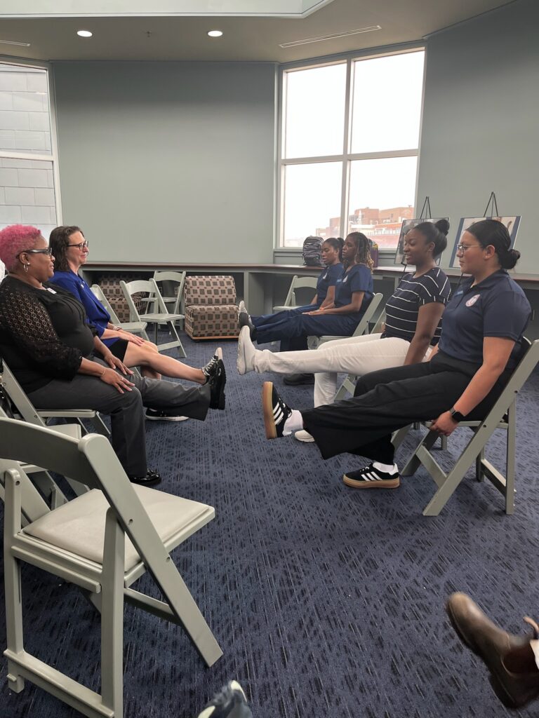 Several women, including Councilmember Nadeau, seated in chairs doing leg raise exercises