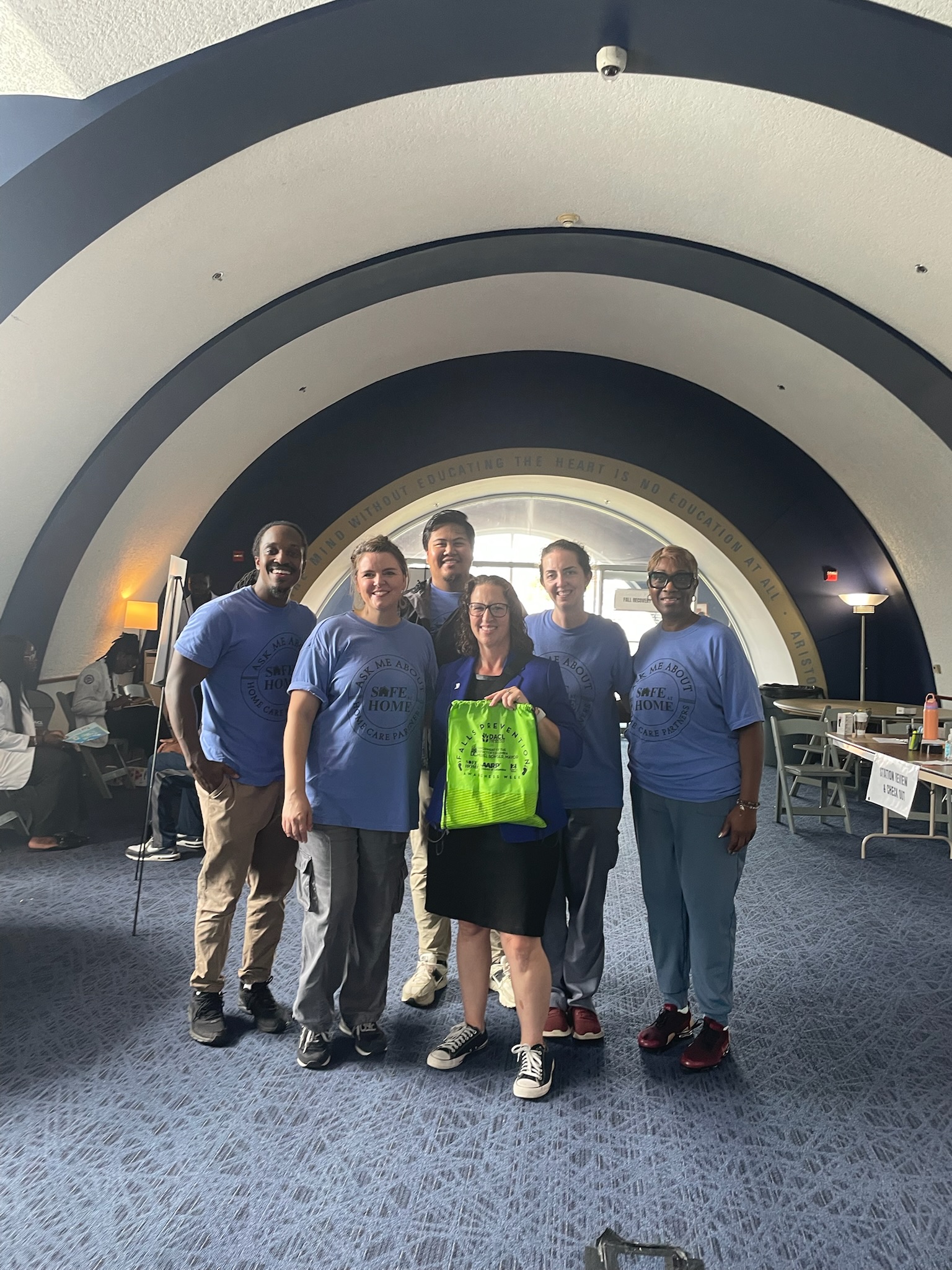 Several people pose for a photo with Councilmember Nadeau, who is holding a lime green drawstring bag