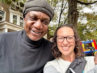 A man and Councilmember Nadeau smile in a selfie photo with a house, a tree, and a bouncy house behind them.