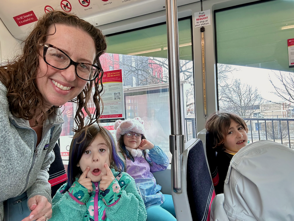 Councilmember Nadeau poses on the streetcar with her children and friends. Her daughter makes a sad face.