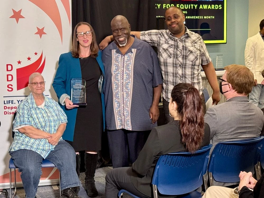 Councilmember Nadeau poses with award, with Ricardo, Donna, and another man at the front of the room.