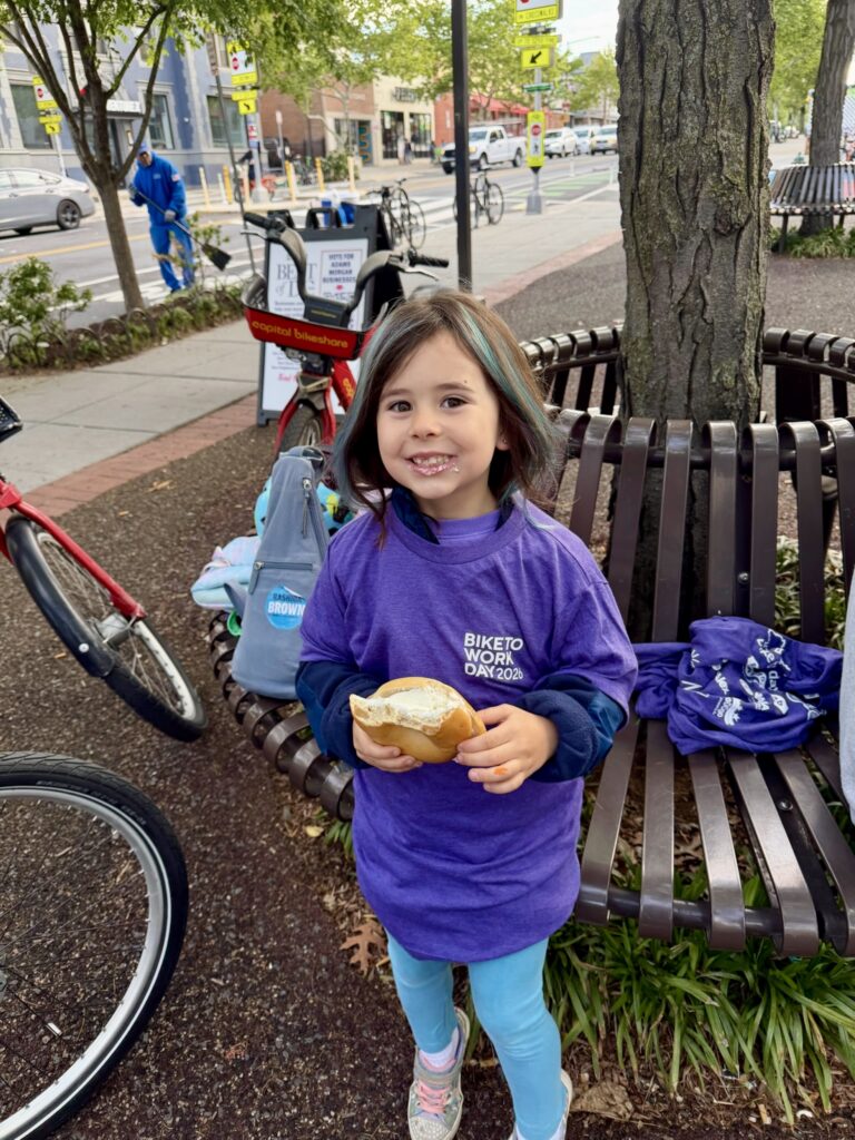 Brianne Nadeau's daughter poses with a bagel in her hand at a Bike to Work pit stop in Adams Morgan