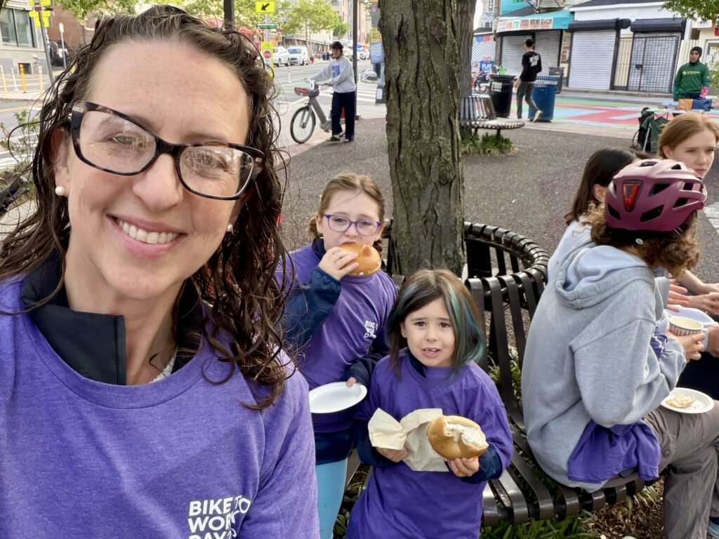 Brianne Nadeau and her daughters, who are eating bagels, pose for a selfie at a Bike to Work pit stop in Adams Morgan