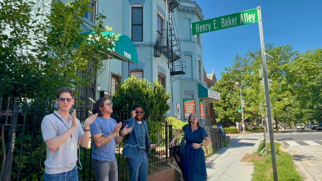 Several people clapping next to the new Henry E. Baker Alley street sign.