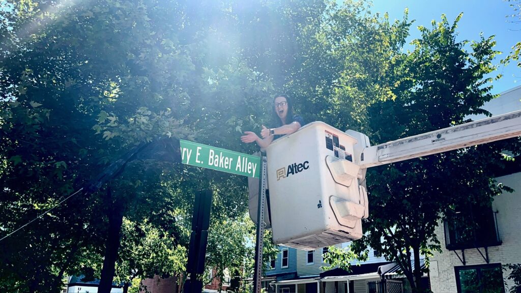 Councilmember Nadeau in a cherry picker next to the new street sign: "Henry E. Baker Alley"