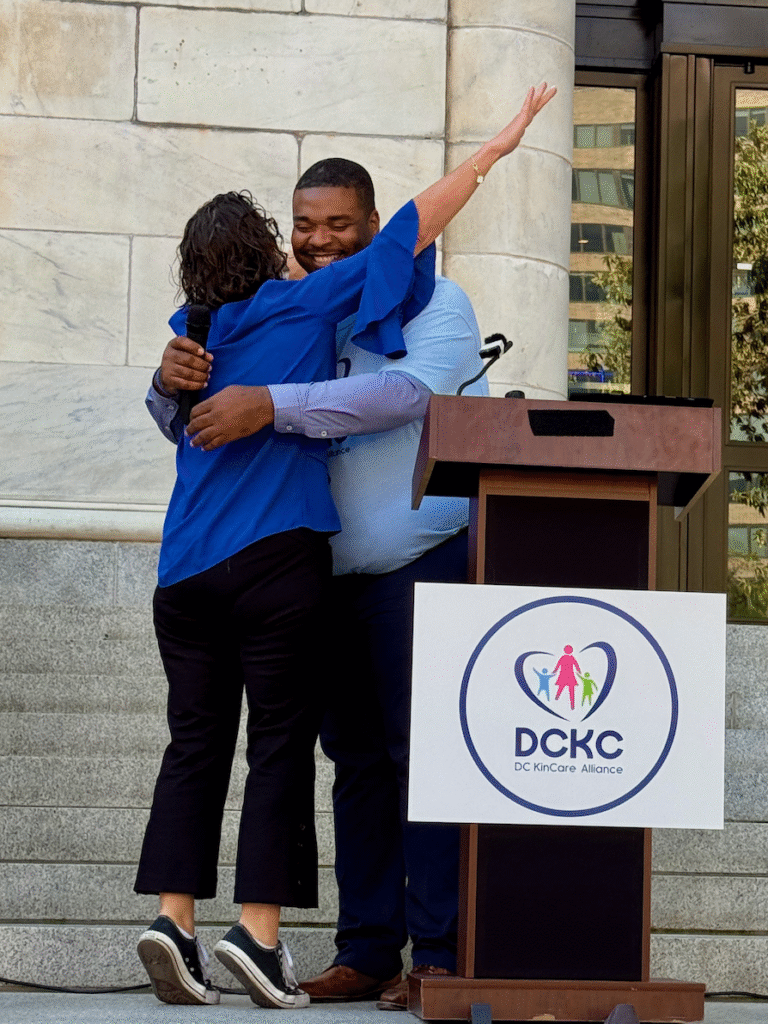 Councilmember Nadeau hugs a man who is standing behind a DC Kincare alliance podium