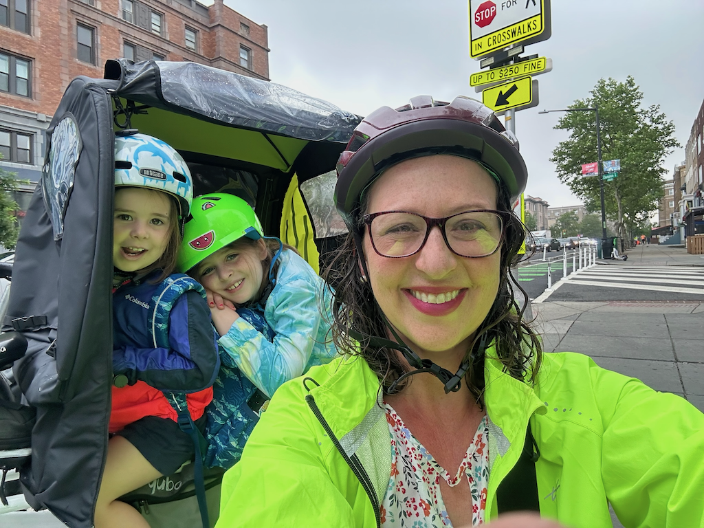 Brianne Nadeau on her e-bike with her two kids, all wearing helmets