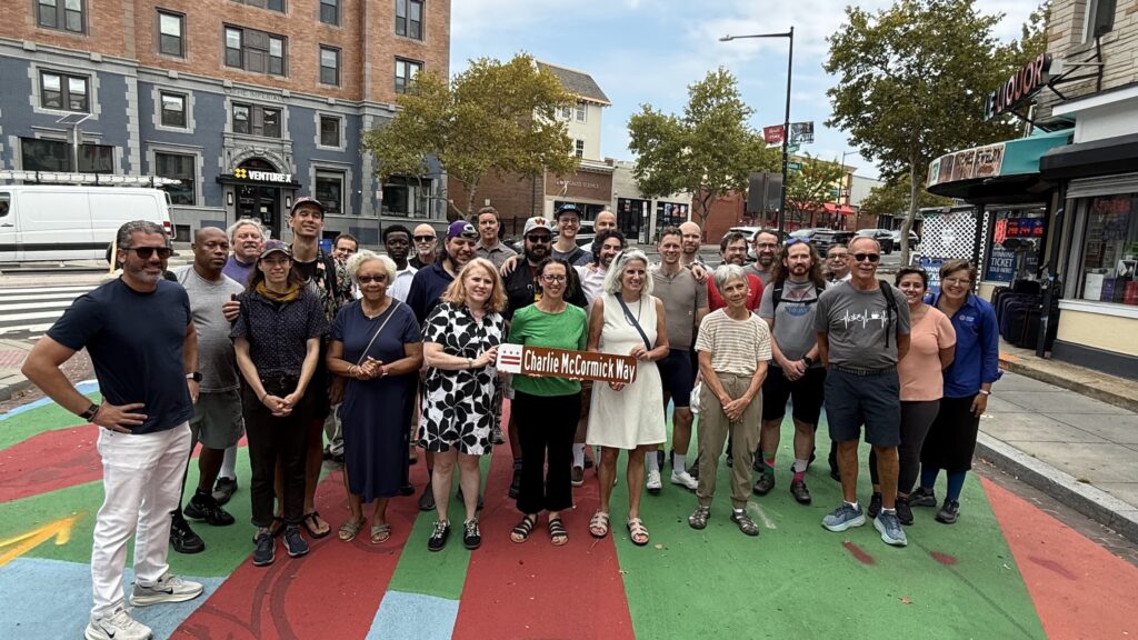 Gathering of people at the Charlie McCormick Way sign unveiling. Three women in the front hold the street sign