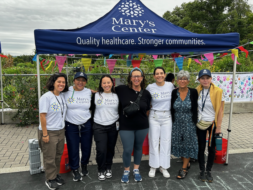 Seven women pose under a tent that says Mary's Center Quality Healthcare. Stronger communities.